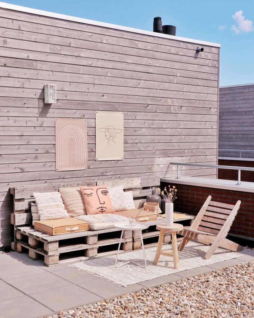 een palletbank staat voor een houten muur op een ruim balkon