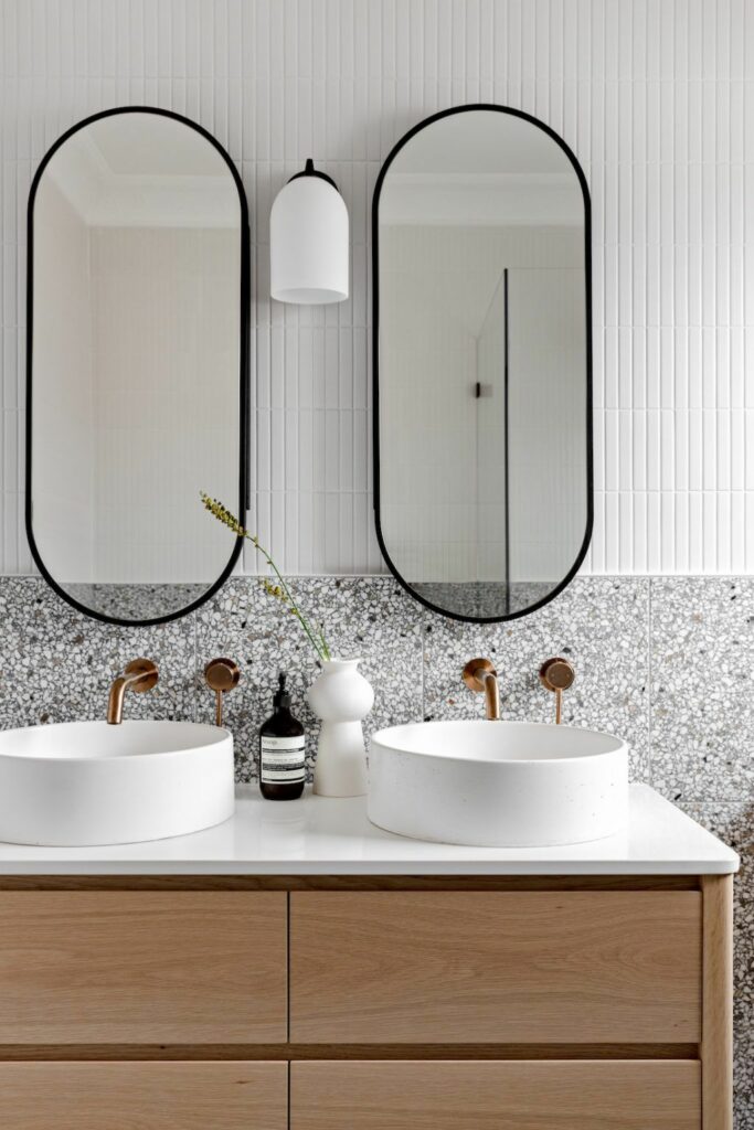 Een wastafel in een badkamer met twee ovale spiegels 