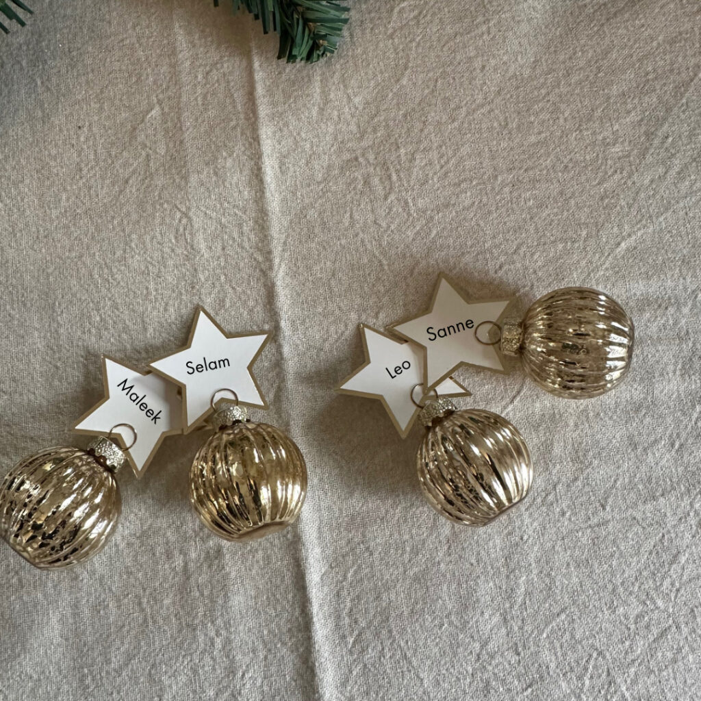 kleine kerstballen met naamkaartje op een beige tafelkleed